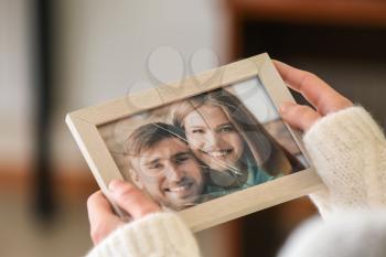 Woman holding photo of happy couple in frame with cracked glass, closeup. Concept of divorce�