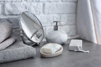 Soap with towels and mirror on grey table in bathroom�
