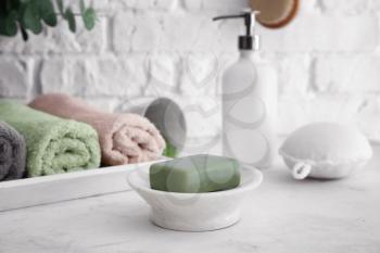 Dish with soap and rolled towels on light table in bathroom�