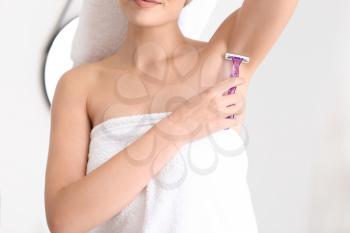 Beautiful young woman shaving armpits in bathroom�