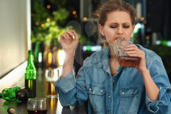 Depressed young woman drinking alcohol in bar�