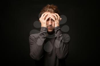 Young man suffering from headache on dark background�
