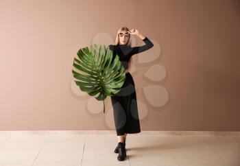 Beautiful woman with green tropical leaf near color wall�