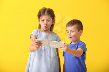 Cute little children playing with smartphones on color background�