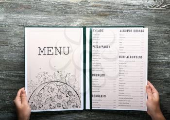 Female hands with menu on wooden table�
