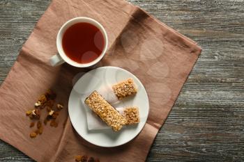 Plate with tasty granola bars and cup of tea on wooden background�