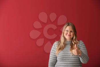 Beautiful plus size girl showing thumb-up gesture on color background. Concept of body positivity�