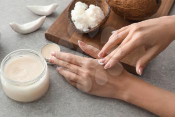 Woman applying coconut oil onto skin on grey background�