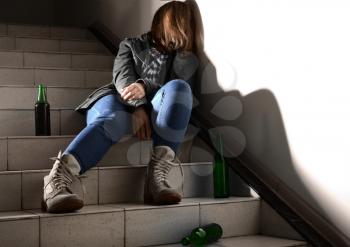 Unconscious young woman with empty bottles sitting on stairs. Concept of alcoholism�