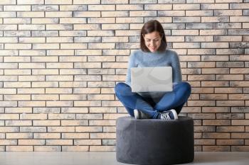Young woman working with laptop while sitting near brick wall�
