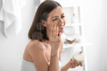 Young woman applying coconut oil in bathroom�