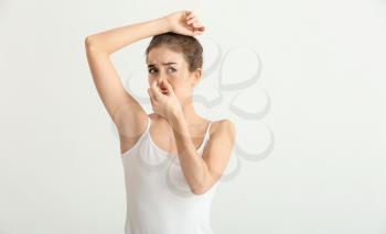 Beautiful young woman feeling smell of sweat on light background. Concept of using deodorant�
