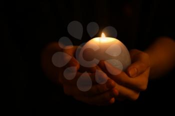 Female hands with burning candle in darkness�