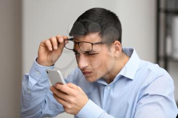 Young man with bad sight trying to read message on screen of mobile phone�