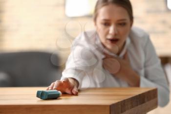 Young woman with asthma attack taking inhaler from table�