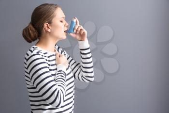 Young woman with inhaler having asthma attack on grey background�