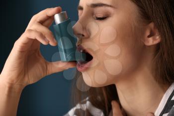 Young woman with inhaler having asthma attack on color background, closeup�