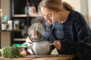 Woman with saucepan of tasty hot soup in kitchen�