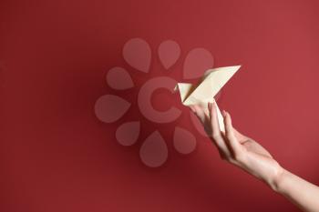 Female hand with origami bird on color background�