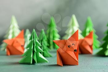 Origami foxes with fir trees on color table�