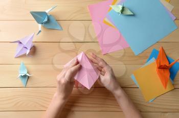 Young woman making origami on wooden table�