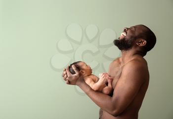 Portrait of happy African-American father with little baby on color background�