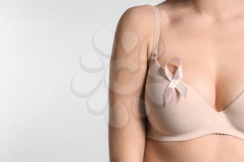 Young woman with beautiful breast and pink ribbon on light background. Cancer awareness concept�