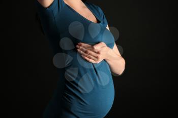 Pregnant woman touching her breast on dark background�