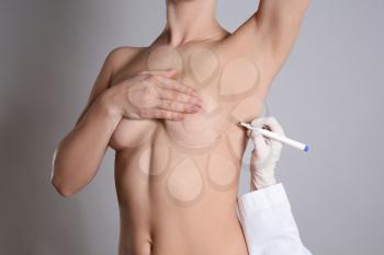 Doctor drawing marks on female breast before cosmetic surgery operation against grey background�