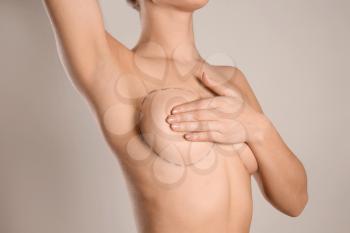 Young woman with marks on breast for cosmetic surgery operation against grey background�