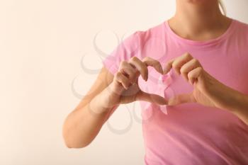 Woman with pink ribbon making heart with hands on light background. Breast cancer awareness concept�