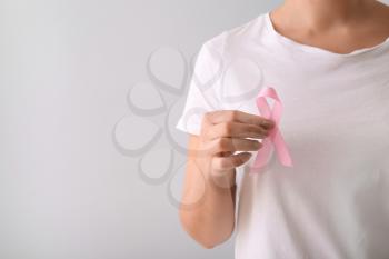 Woman with pink ribbon on light background. Breast cancer awareness concept�