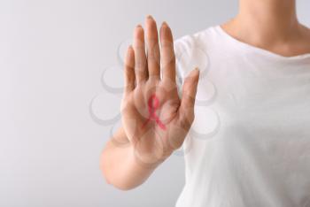 Woman with pink ribbon drawn on her palm against light background. Breast cancer awareness concept 