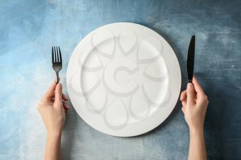 Female hands with cutlery and empty plate on color background�