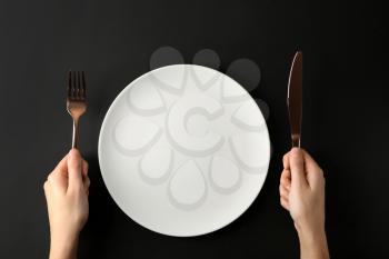 Female hands with cutlery and empty plate on dark background 