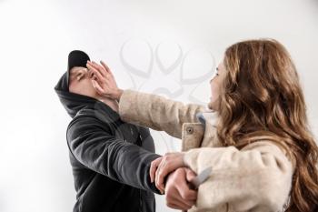 Young woman defending herself from thief on light background�