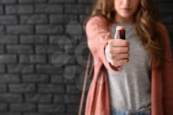 Woman with pepper spray for self-defence against dark brick wall�