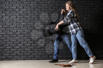 Young woman defending herself from attack by thief near dark brick wall�