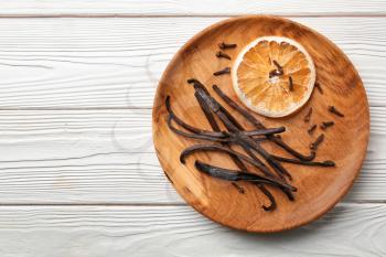 Plate with dry orange slice and aromatic vanilla sticks on white wooden background�