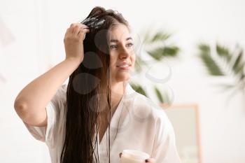 Young woman applying cream on beautiful long hair in bathroom�