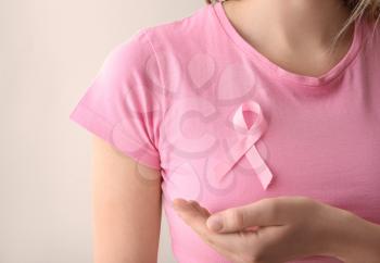 Woman with pink ribbon on light background, closeup. Breast cancer awareness concept�