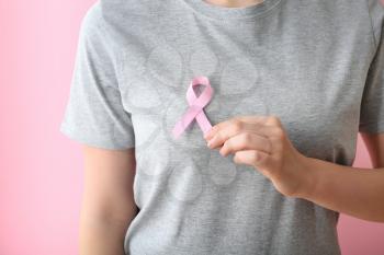 Woman with pink ribbon on color background, closeup. Breast cancer awareness concept�