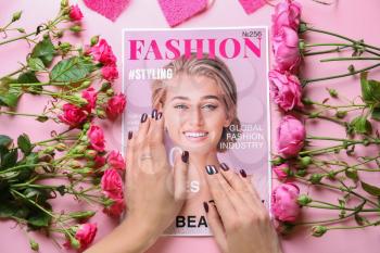 Female hands with fashionable magazine and flowers on color background�