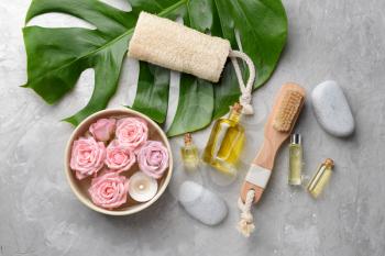 Spa composition with cosmetics, flowers and tropical leaf on grey background�