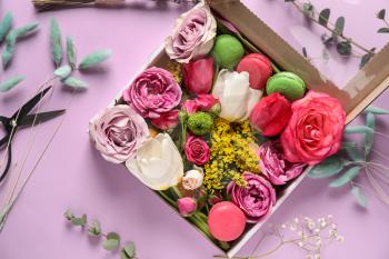 Gift box with beautiful flowers and macarons on color background�