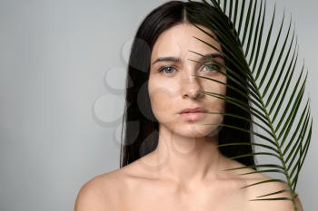 Portrait of beautiful young woman with natural makeup and tropical leaf on grey background�