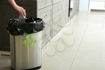 Young woman throwing empty plastic bottle into trash bin at home. Recycle concept�
