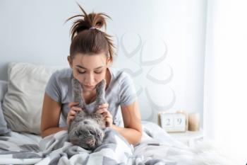 Young woman with cute cat resting on bed at home�