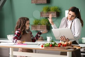 Stressed busy mother with daughter working in kitchen at home�