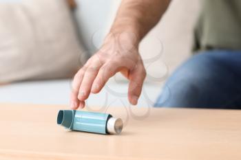 Young man with asthma attack taking inhaler from table, closeup�